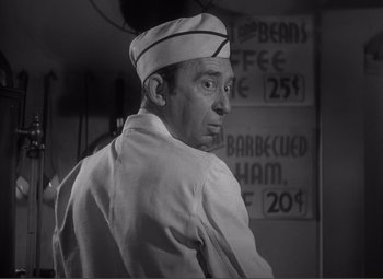 Movie still from “Sullivan's Travels” (1941), directed by Preston Sturges – A man wearing a white hat standing in front of signs; Close Up shot, Low angle