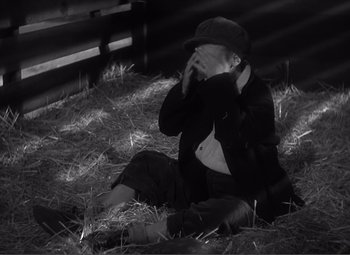 Movie still from “Sullivan's Travels” (1941), directed by Preston Sturges – A person sitting on the ground with hay in the background; Medium shot, High angle