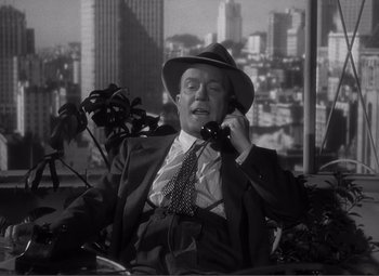 Movie still from “Sullivan's Travels” (1941), directed by Preston Sturges – A man in a suit and hat talking on a phone; Medium shot, High angle
