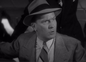Movie still from “Sullivan's Travels” (1941), directed by Preston Sturges – A man wearing a suit and a hat in a black and white photo; Close Up shot, High angle