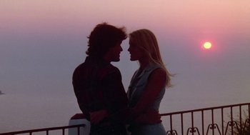 Movie still from “Summer Lovers” (1982), directed by Randal Kleiser – A man and a woman holding each other in front of a sunset; Medium shot, Low angle