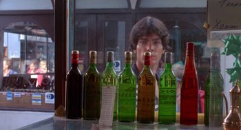 Movie still from “Summer Lovers” (1982), directed by Randal Kleiser – A man sitting in front of a row of bottles; Close Up shot, Low angle