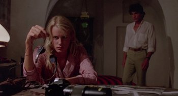 Movie still from “Summer Lovers” (1982), directed by Randal Kleiser – A woman sitting in front of a camera in a room; Medium shot, Low angle