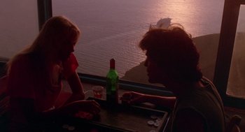 Movie still from “Summer Lovers” (1982), directed by Randal Kleiser – Two people sitting at a table with a bottle of wine; Wide shot, Over the shoulder angle