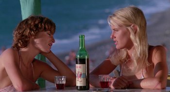 Movie still from “Summer Lovers” (1982), directed by Randal Kleiser – Two women sitting at a table with a bottle of wine; Medium shot, Low angle