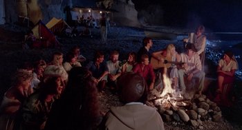 Movie still from “Summer Lovers” (1982), directed by Randal Kleiser – A group of people sitting around a campfire; Wide shot, High angle