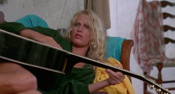 Movie still from “Summer Lovers” (1982), directed by Randal Kleiser – A woman sitting in a chair holding a guitar; Medium shot, High angle