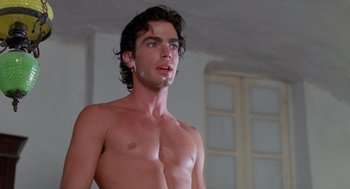 Movie still from “Summer Lovers” (1982), directed by Randal Kleiser – A shirtless man with curly brown hair and white ear buds; Close Up shot, Low angle