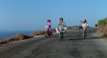 Movie still from “Summer Lovers” (1982), directed by Randal Kleiser – A man and a woman riding a bike down a road; Wide shot, Low angle
