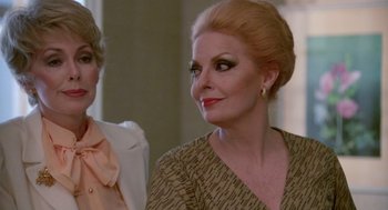 Movie still from “Summer Lovers” (1982), directed by Randal Kleiser – A woman in a brown and white dress looking at the camera; Close Up shot, Over the shoulder angle