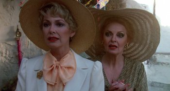 Movie still from “Summer Lovers” (1982), directed by Randal Kleiser – Two older women wearing hats and one is wearing a bow tie; Close Up shot, Over the shoulder angle