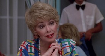Movie still from “Summer Lovers” (1982), directed by Randal Kleiser – An older woman is sitting in front of a group of people; Close Up shot, Over the shoulder angle