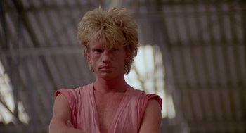 Movie still from “Summer Lovers” (1982), directed by Randal Kleiser – A man in a pink shirt is posing for a picture; Close Up shot, Low angle