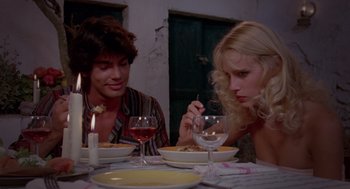 Movie still from “Summer Lovers” (1982), directed by Randal Kleiser – A man and a woman sitting at a dinner table; Medium shot, High angle