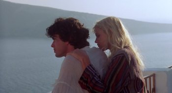 Movie still from “Summer Lovers” (1982), directed by Randal Kleiser – A man and a woman standing next to each other near a body of water; Medium shot, Low angle