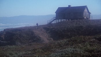 Movie still from “Summer of '42” (1971), directed by Robert Mulligan – A person standing on a hill near a house on the beach; Extreme Wide shot, Low angle