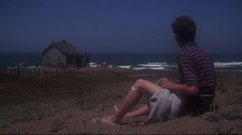 Movie still from “Summer of '42” (1971), directed by Robert Mulligan – A man sitting on the ground near the ocean; Wide shot, High angle