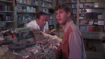 Movie still from “Summer of '42” (1971), directed by Robert Mulligan – A man and a man standing in front of a counter; Medium shot, Over the shoulder angle