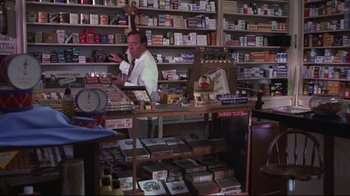 Movie still from “Summer of '42” (1971), directed by Robert Mulligan – A man is standing behind a counter in a store; Medium shot, High angle