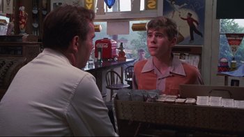 Movie still from “Summer of '42” (1971), directed by Robert Mulligan – Two men sitting at a table in front of each other; Medium shot, Over the shoulder angle