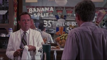 Movie still from “Summer of '42” (1971), directed by Robert Mulligan – A man in a white lab coat is talking to a man in a purple shirt; Medium shot, Over the shoulder angle