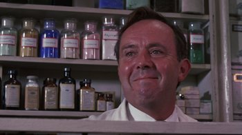 Movie still from “Summer of '42” (1971), directed by Robert Mulligan – A man sitting in front of a shelf filled with bottles; Close Up shot, Low angle