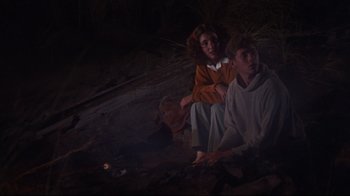 Movie still from “Summer of '42” (1971), directed by Robert Mulligan – Two people sitting on the ground near a fire; Medium shot, Low angle