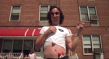 Movie still from “Summer of Sam” (1999), directed by Spike Lee – A man in a t - shirt is standing in front of a brick building; Medium shot, Low angle