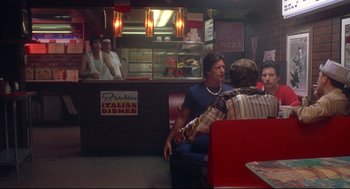 Movie still from “Summer of Sam” (1999), directed by Spike Lee – A man sitting in a booth at an italian restaurant; Wide shot, Over the shoulder angle