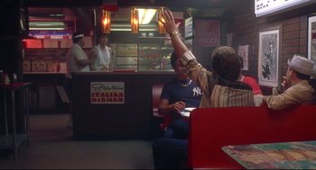 Movie still from “Summer of Sam” (1999), directed by Spike Lee – Two people sitting at a table in front of a counter; Wide shot, Low angle
