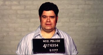 Movie still from “Summer of Sam” (1999), directed by Spike Lee – A man in a blue shirt is in front of a white brick wall; Medium shot, Low angle