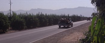 Movie still from “Sunset” (1988), directed by Blake Edwards – A group of people riding in the back of a truck down a road; Extreme Wide shot, High angle