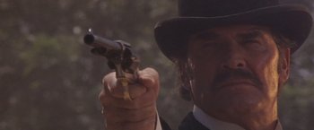 Movie still from “Sunset” (1988), directed by Blake Edwards – A man in a top hat holding a gun in his hand; Close Up shot, Low angle