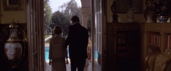 Movie still from “Sunset” (1988), directed by Blake Edwards – A man and a woman holding hands while standing in front of an open door; Wide shot, Low angle