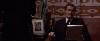 Movie still from “Sunset” (1988), directed by Blake Edwards – An older man sitting in a chair next to a woman holding a book; Medium shot, Over the shoulder angle