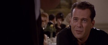 Movie still from “Sunset” (1988), directed by Blake Edwards – A person sitting at a table in front of other people; Close Up shot, Over the shoulder angle