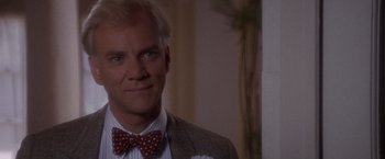 Movie still from “Sunset” (1988), directed by Blake Edwards – A man in a suit and bow tie smiling for the camera; Close Up shot, Over the shoulder angle