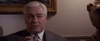 Movie still from “Sunset” (1988), directed by Blake Edwards – An older man wearing a suit and tie in front of a painting; Close Up shot, Over the shoulder angle