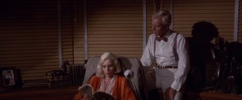 Movie still from “Sunset” (1988), directed by Blake Edwards – A man and a woman sitting in a chair reading a book; Medium shot, High angle