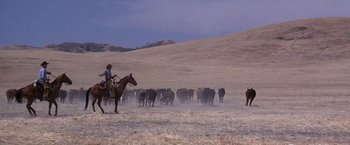 Movie still from “Sunset” (1988), directed by Blake Edwards – A man on horseback herds a herd of cattle; Extreme Wide shot, Low angle
