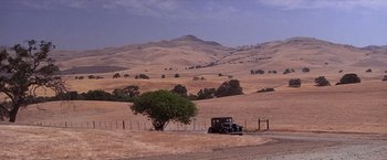Movie still from “Sunset” (1988), directed by Blake Edwards – An old car is parked on the side of the road near a tree; Extreme Wide shot, High angle