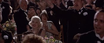Movie still from “Sunset” (1988), directed by Blake Edwards – A group of people sitting at a table in front of a crowd; Medium shot, Low angle