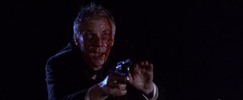 Movie still from “Sunset” (1988), directed by Blake Edwards – A man with blood all over his face holding a gun in the dark; Close Up shot, Low angle