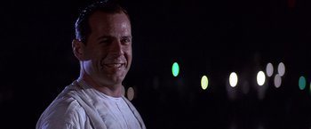 Movie still from “Sunset” (1988), directed by Blake Edwards – A man smiles at the camera in front of some lights; Close Up shot, Low angle