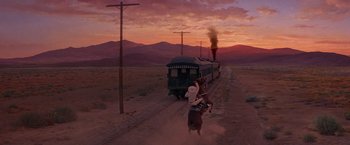 Movie still from “Sunset” (1988), directed by Blake Edwards – A train traveling down train tracks next to a dirt field; Extreme Wide shot, Low angle