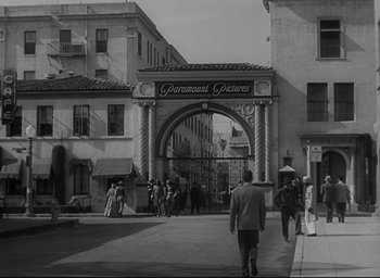 Movie still from “Sunset Blvd.” (1950), directed by Billy Wilder – A black - and - white photo of people walking down a street; Extreme Wide shot, Over the shoulder angle