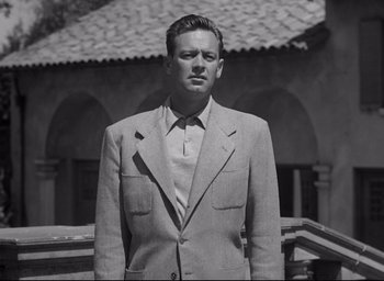 Movie still from “Sunset Blvd.” (1950), directed by Billy Wilder – A man wearing a suit and tie standing in front of a building; Medium shot, Low angle
