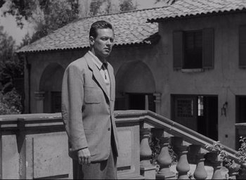Movie still from “Sunset Blvd.” (1950), directed by Billy Wilder – A black and white photo of a man standing on a balcony; Medium shot, Low angle