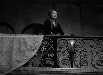 Movie still from “Sunset Blvd.” (1950), directed by Billy Wilder – A woman standing on top of an iron railing holding a wine glass; Medium shot, Low angle