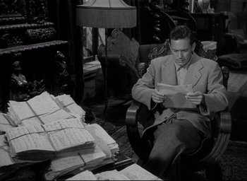 Movie still from “Sunset Blvd.” (1950), directed by Billy Wilder – A black and white photo of a man sitting in a chair reading; Medium shot, High angle